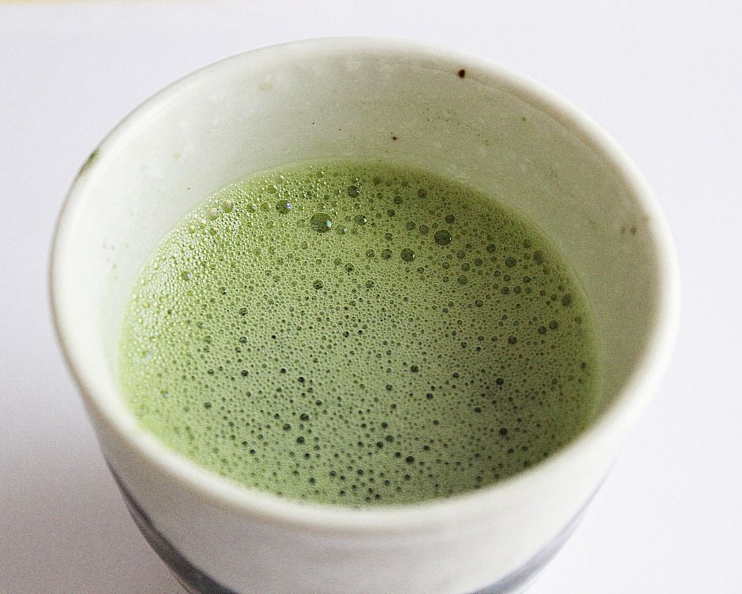Ceramic bowl filled with green matcha tea on a white background