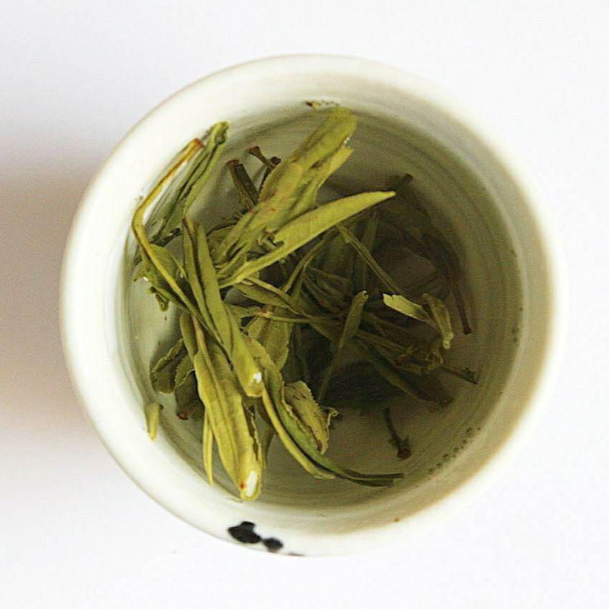 Yellow tea leaves in a white teacup on a white background